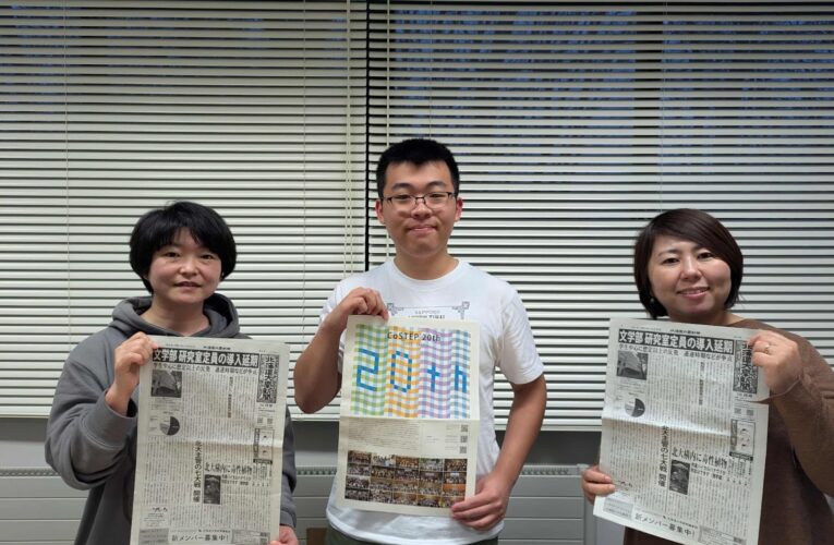 三人の人間が並んでいる画像。それぞれが紙面を持ち笑っている。